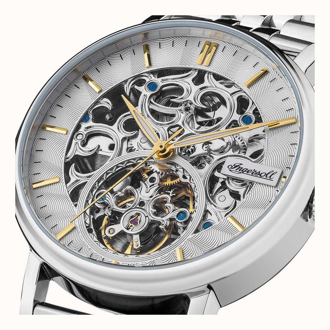 Automatic skeleton watch close-up showing silver gears, blue jewels, and gold hour hands