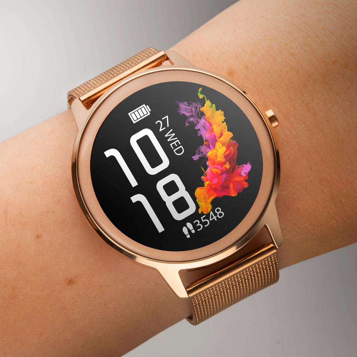 Rose gold smartwatch on wrist with mesh band and round black face showing 10 and 18
