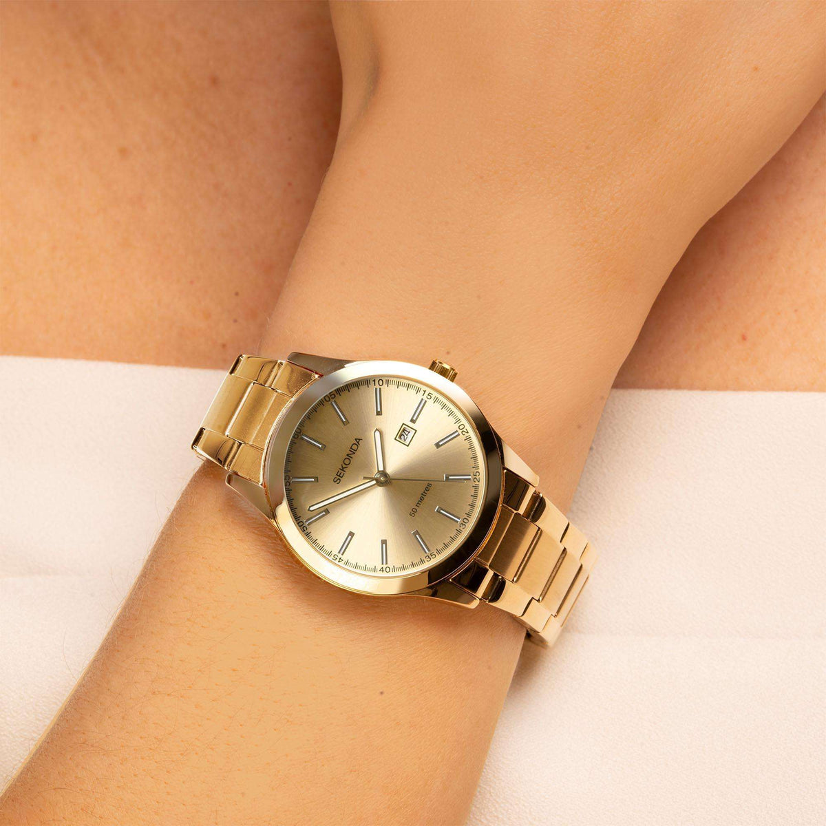 Gold-tone ladies quartz wristwatch on wrist with champagne dial and metal bracelet.