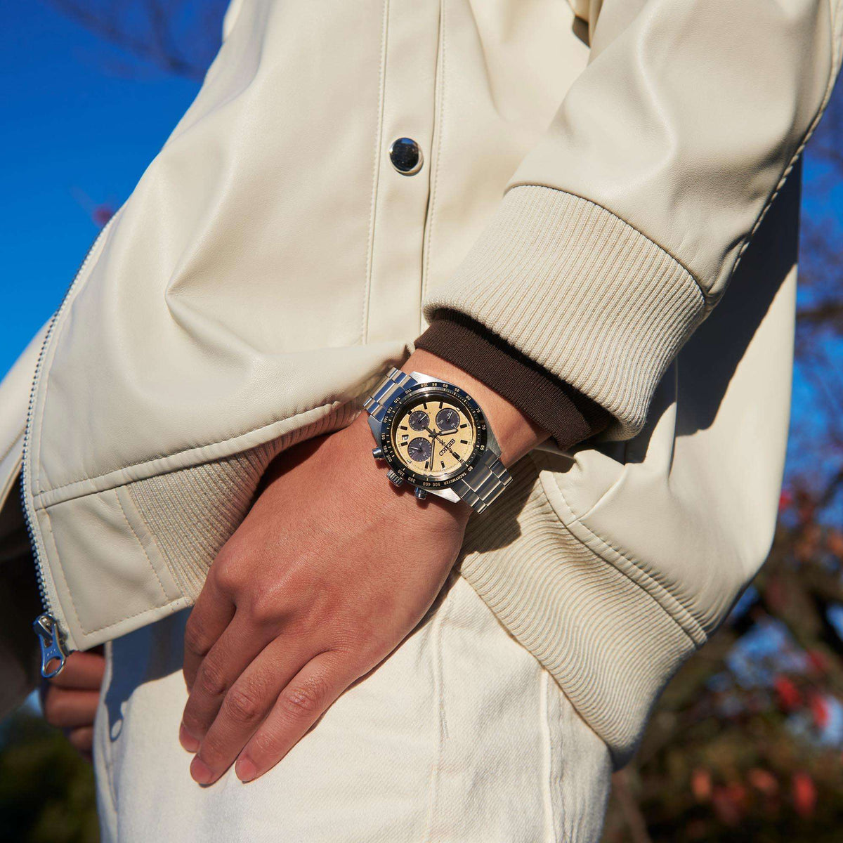 Seiko chronograph watch on wrist with gold dial and steel bracelet under jacket sleeve