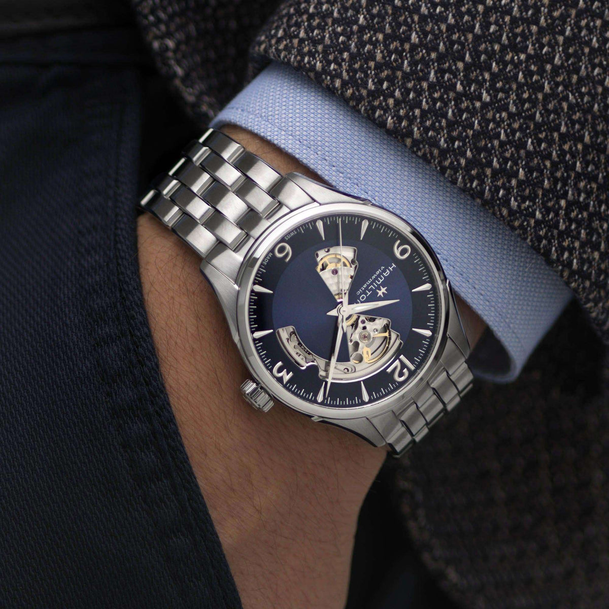 Hamilton Jazzmaster H32705141 mens automatic watch worn on wrist under suit cuff showing blue dial, exposed movement, and steel bracelet