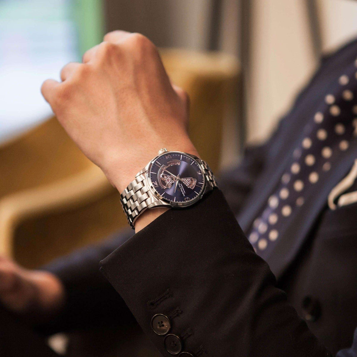 Hamilton Jazzmaster H32705141 automatic watch styled wrist shot with dark blazer showcasing blue open heart dial and steel link bracelet