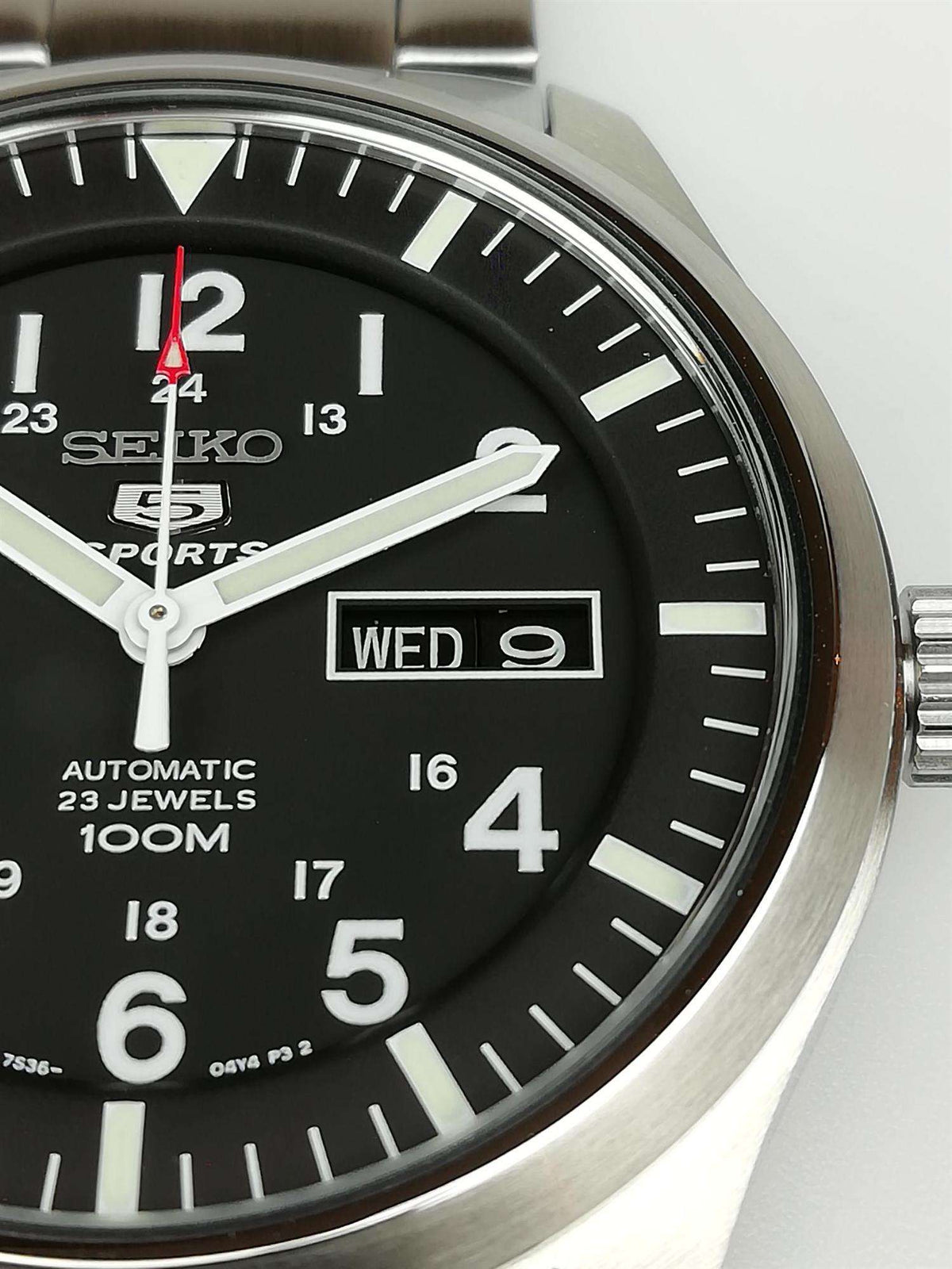 Seiko 5 Sports dial closeup with day-date box, black face, and steel bezel