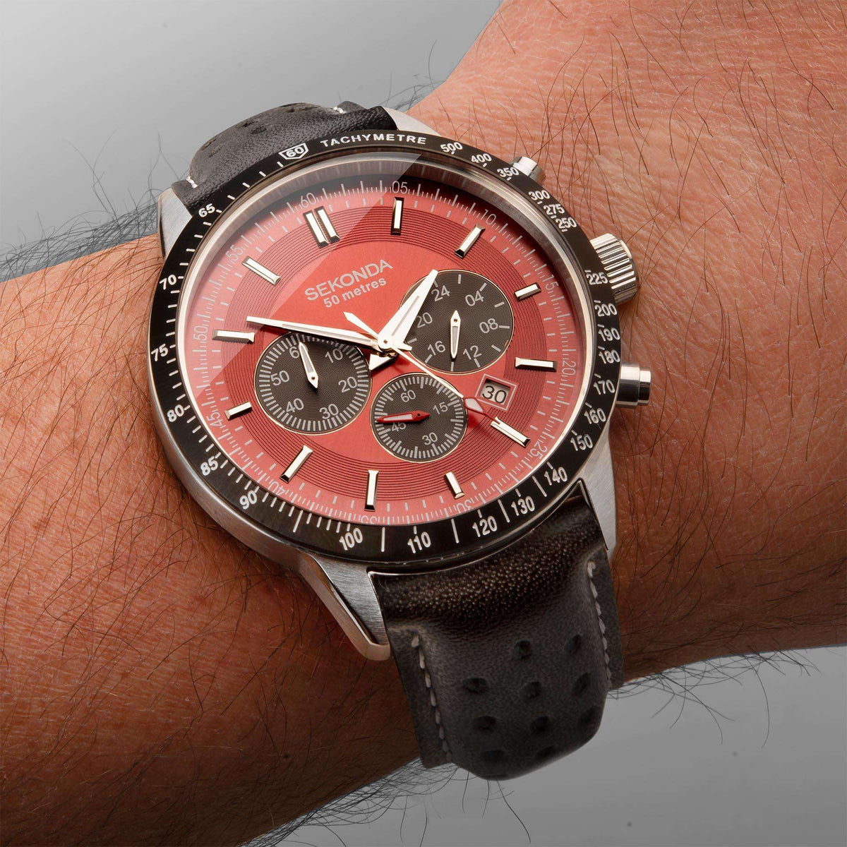 Men's chronograph watch on wrist with red dial, black leather strap, silver case