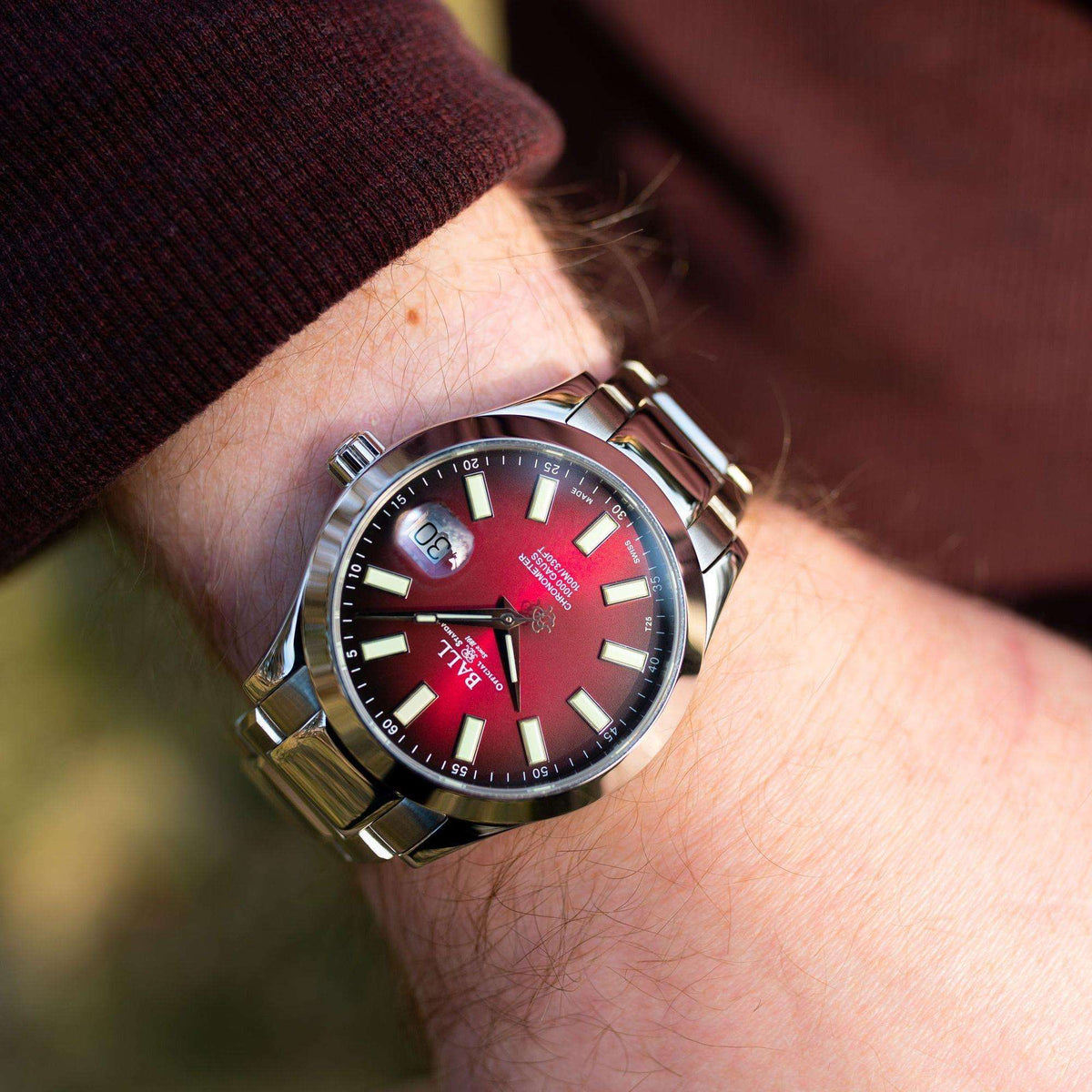 Men's stainless steel watch on wrist, red dial with baton markers and date window