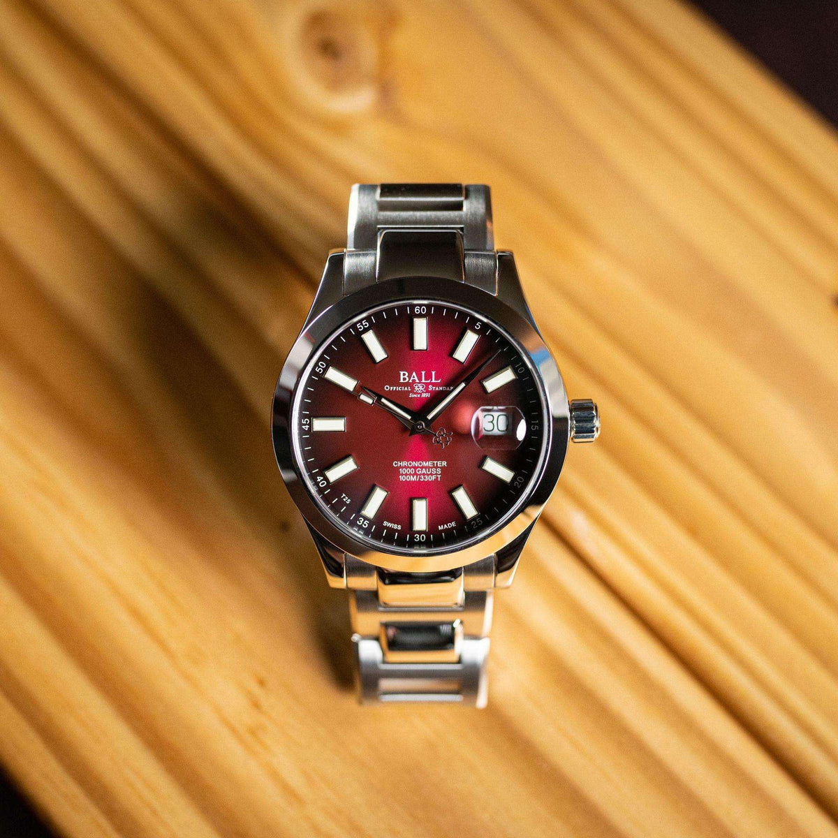 Men's stainless steel watch with red dial and date window, worn on wrist