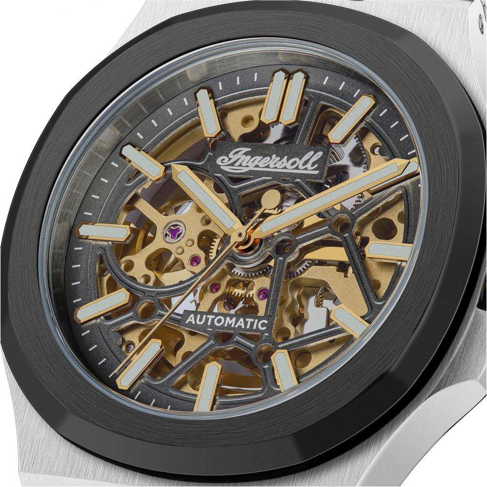 Automatic watch dial close-up with visible gold-toned gears, dark face, and gold hands.