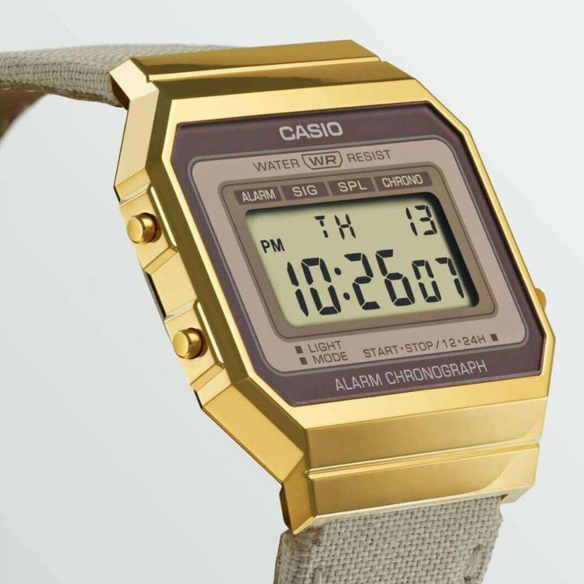 Gold digital watch close-up with LCD time readout on cream fabric strap