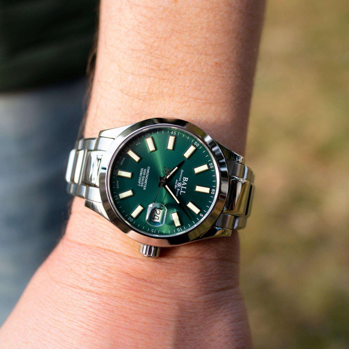Men's wrist watch with dark green dial, stainless steel bracelet, crown side view on wrist.