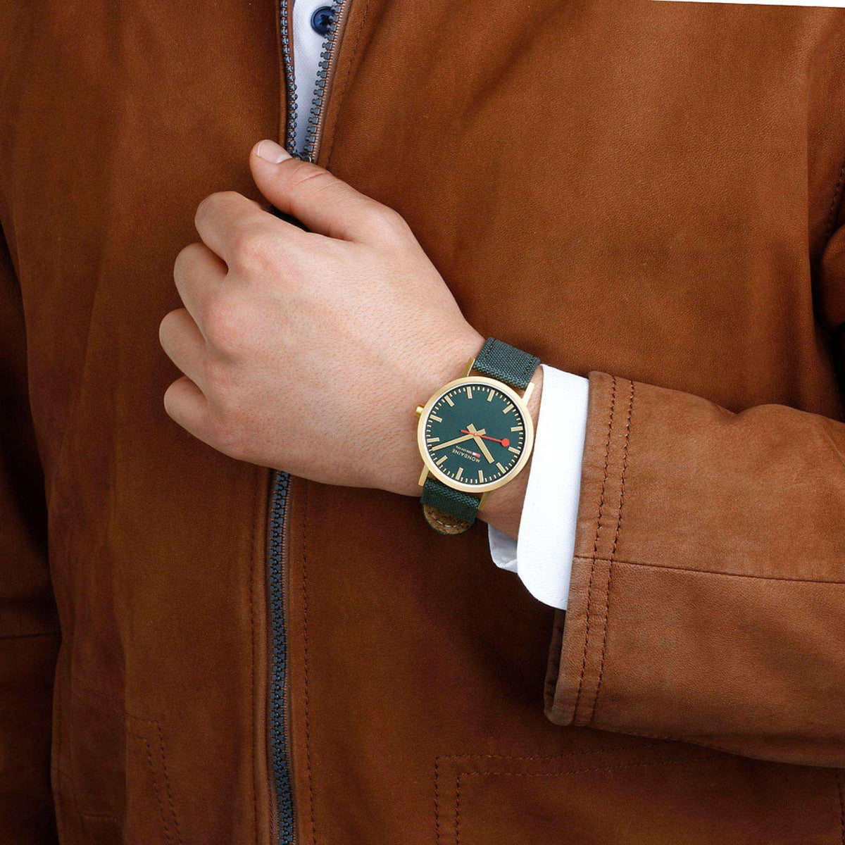 Mondaine watch on wrist with dark green dial, gold-tone case, and green fabric strap