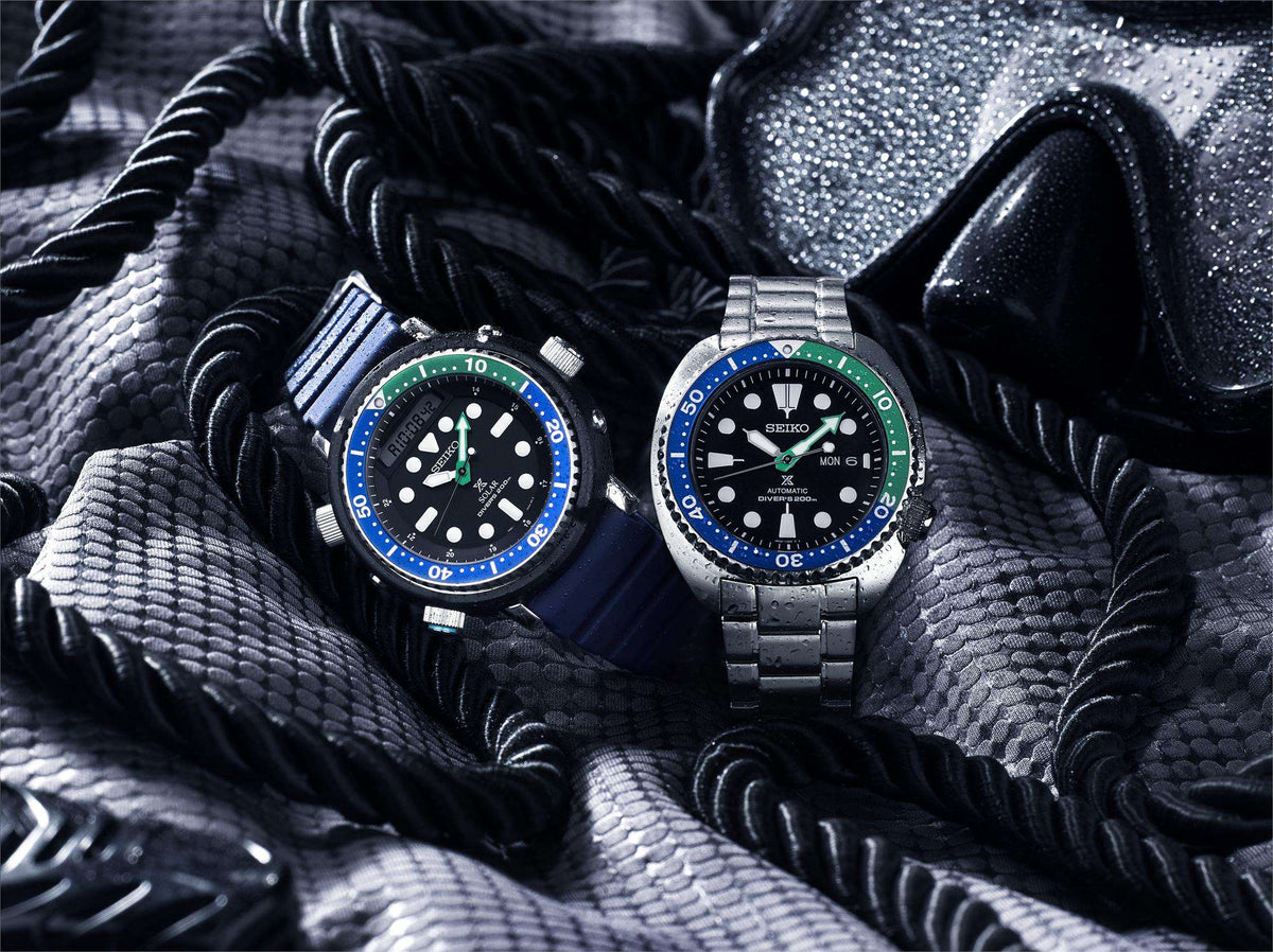 Two men’s diver watches with black dials, blue bezels, and green accents on metal bands