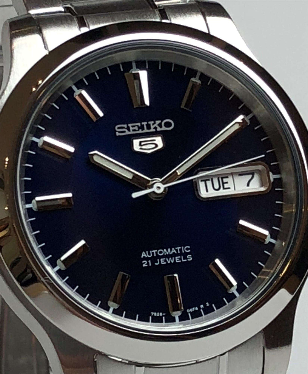 Men's steel automatic watch close-up with blue dial, baton markers, and date window TUE 7