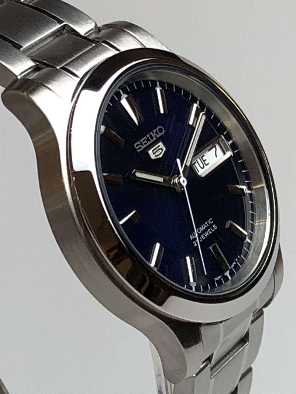 Men's steel automatic watch profile with blue dial, baton hour markers, and date window