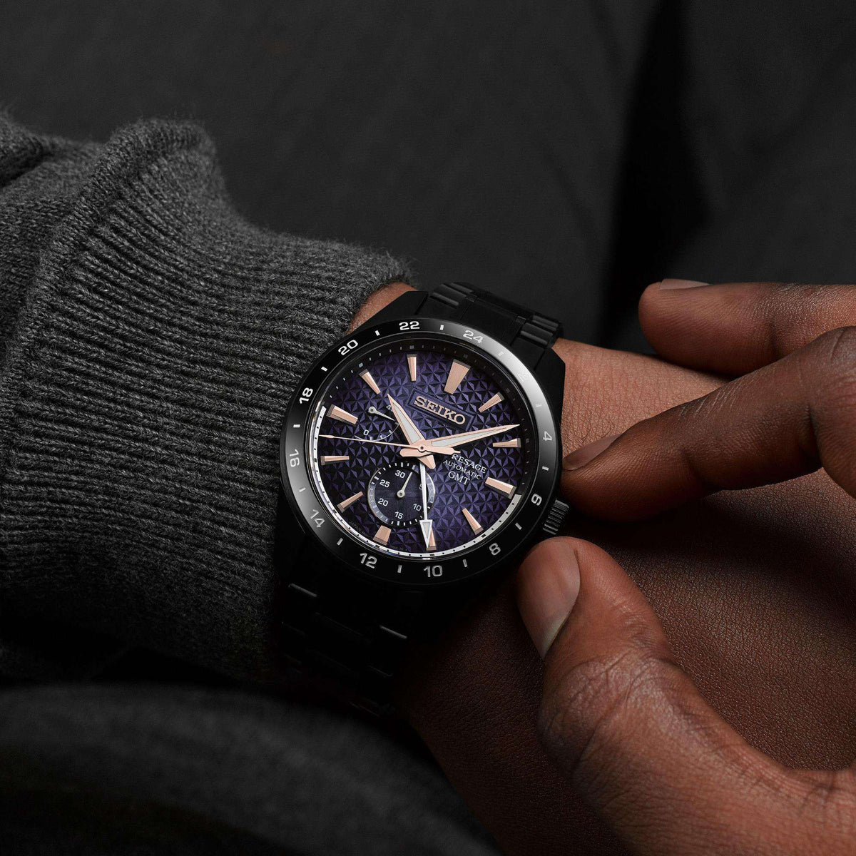 On-wrist the watch paired with a textured grey knit sweater, highlighting the dark violet and blue hues of its geometric dial under lifestyle lighting.