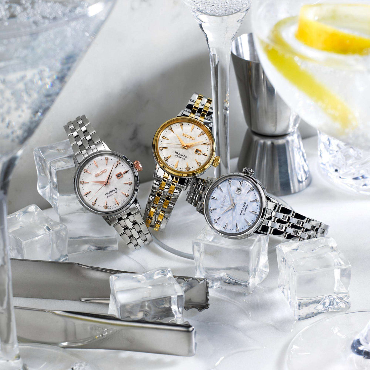 Three distinct Seiko Presage ladies' watches resting on faux ice cubes with cocktail accessories and bar tools around them.