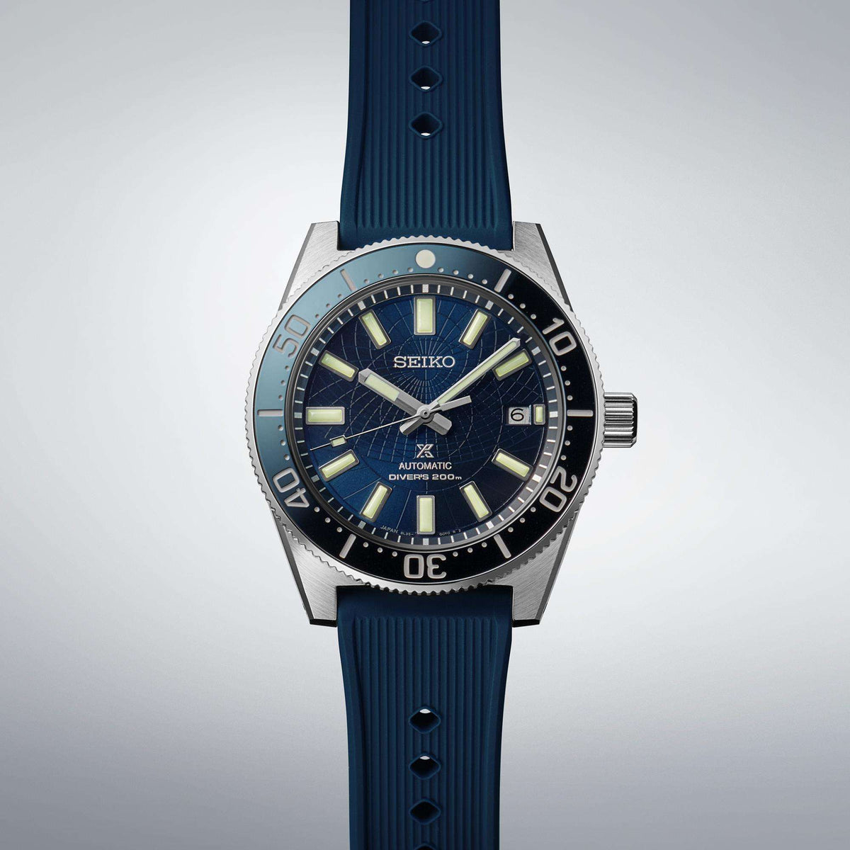 Full studio layout of the watch standing vertically against a light gray gradient background, showing the ribbed texture of the blue silicone strap.