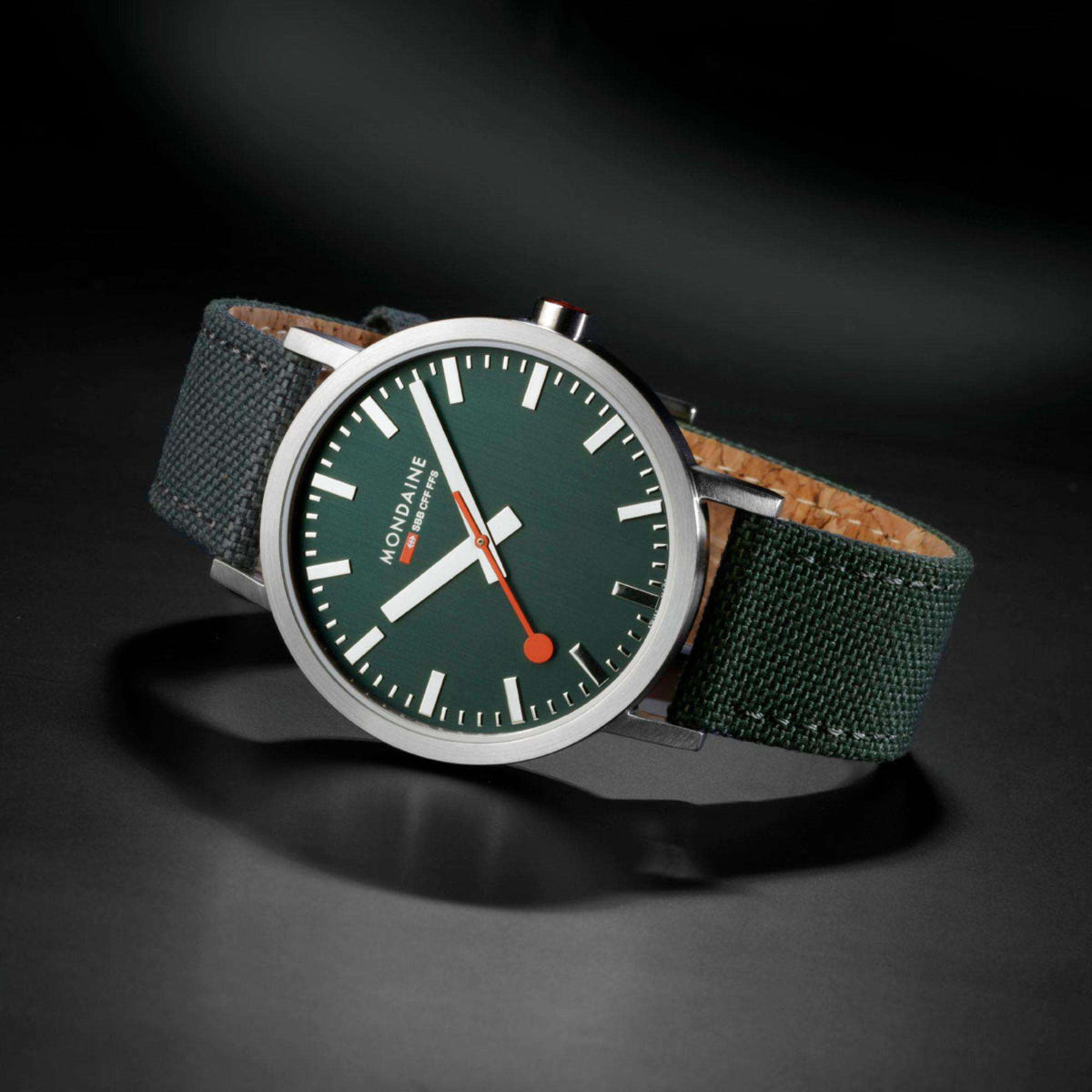 Mondaine Classic wristwatch angled on green fabric strap with forest green dial and silver case.