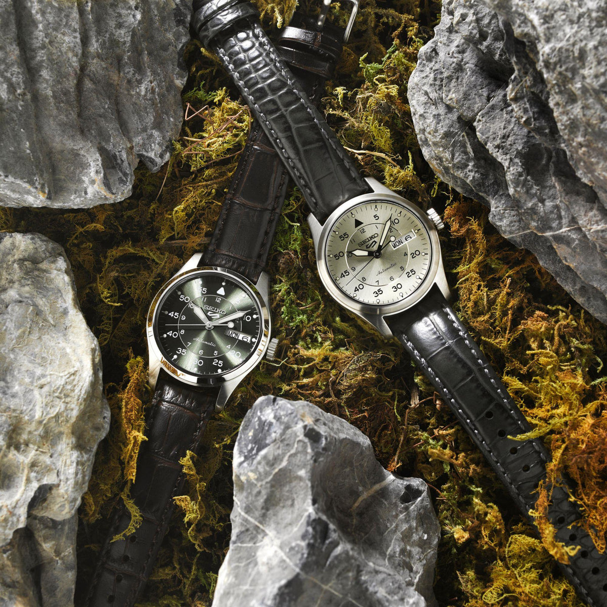 Two Seiko 5 Sports pilot watches with black leather straps on rocks, one with champagne dial