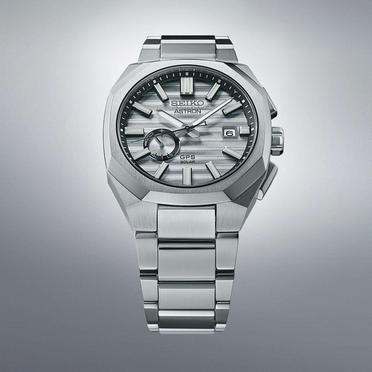 Front view of the watch against a gradient grey background, showcasing its titanium case and octagonal bezel.