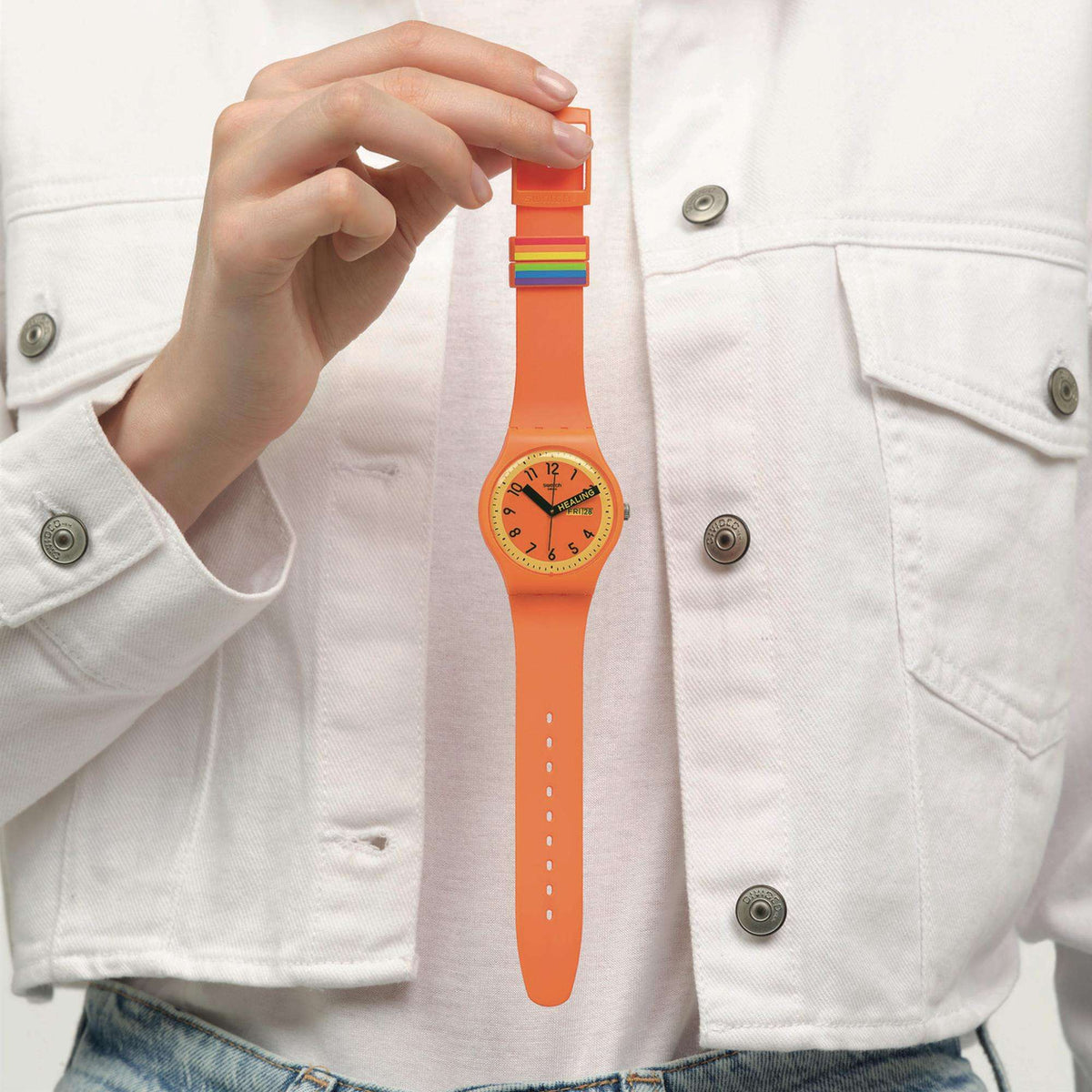 Orange quartz watch on wrist with silicone strap; hand adjusting the buckle near top