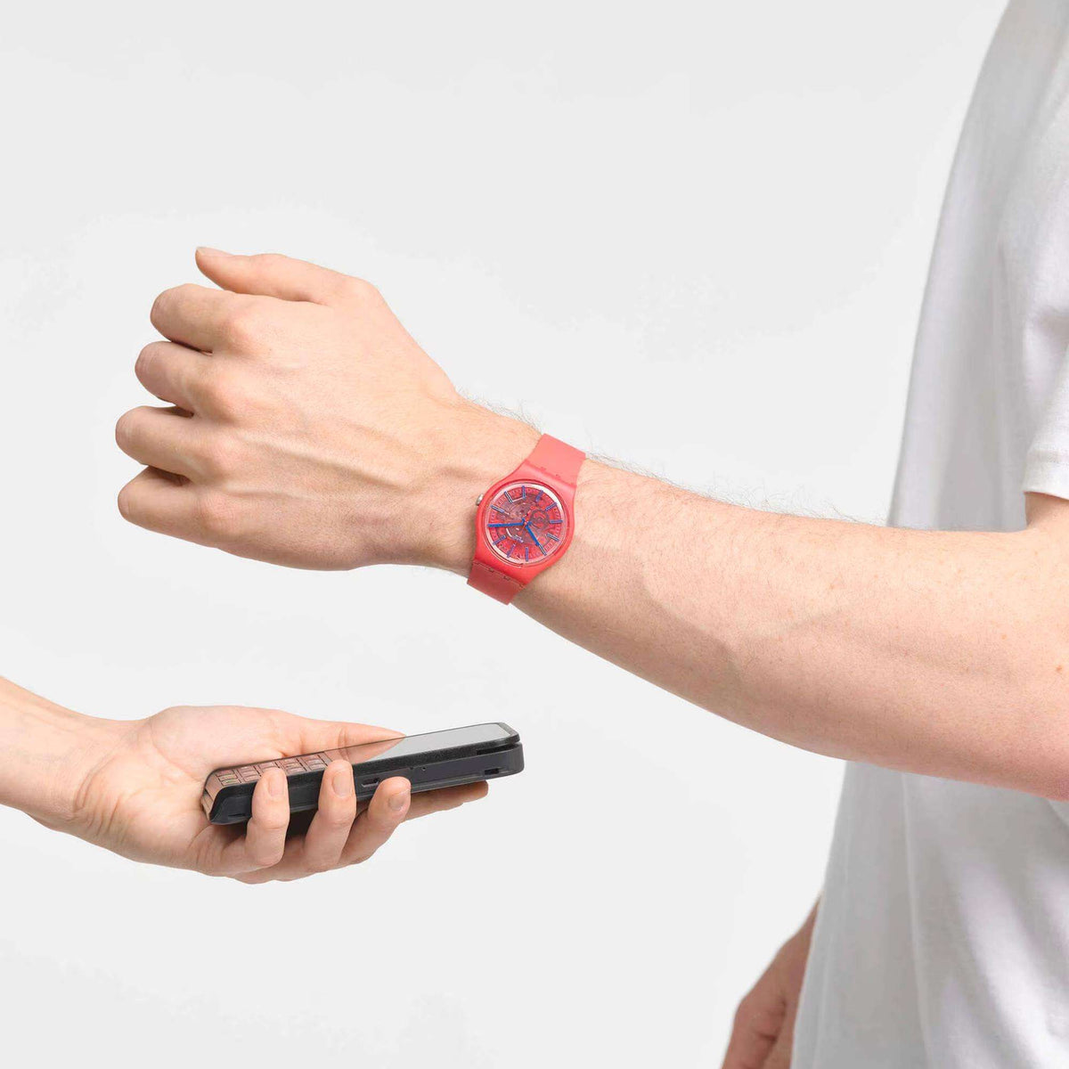 Red dial Swatch quartz watch on wrist, silicone strap visible while holding smartphone