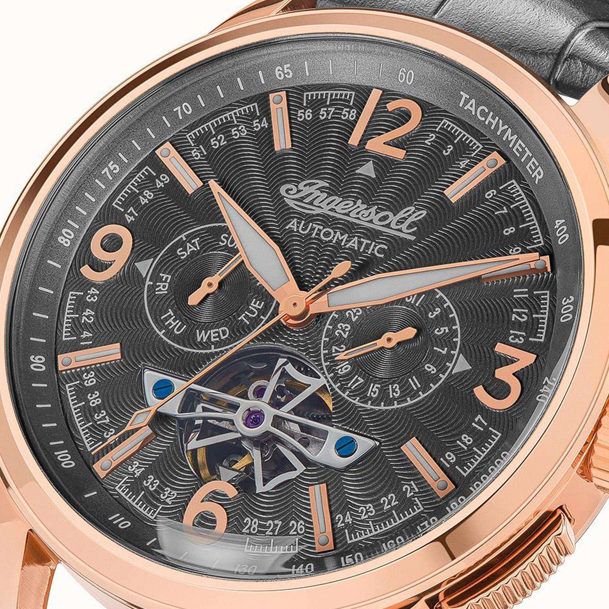 Ingersoll automatic watch close-up: black dial, skeleton movement, tachymeter, rose-gold case.