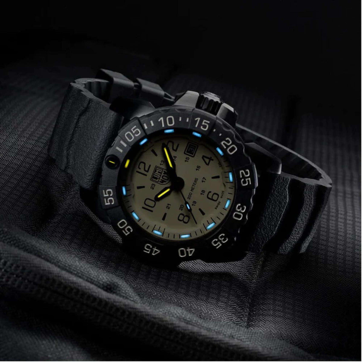 Angled men's dive watch with black bezel and glowing blue-yellow luminous dial on black strap.