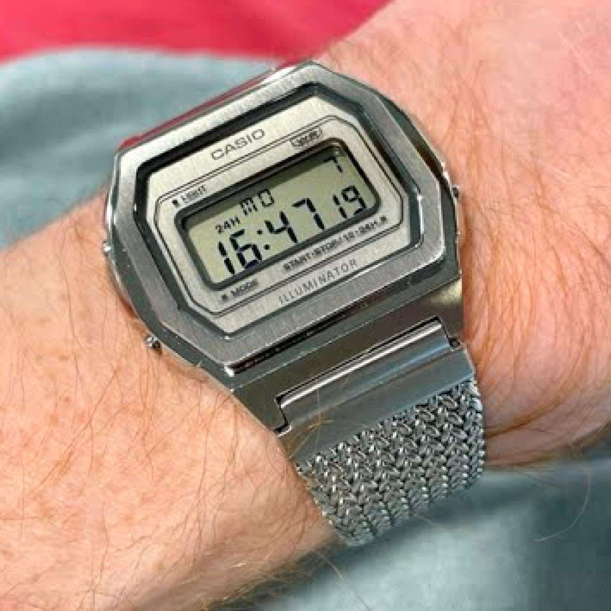 Casio stainless steel digital watch on wrist with textured metal mesh band and LCD display