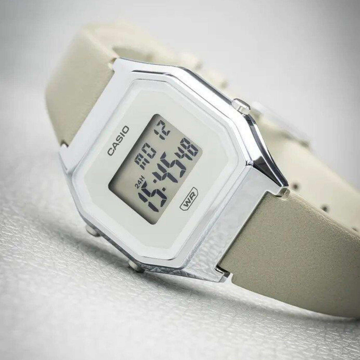 Casio digital watch close-up with grey leather strap, LCD showing date/time and WR mark