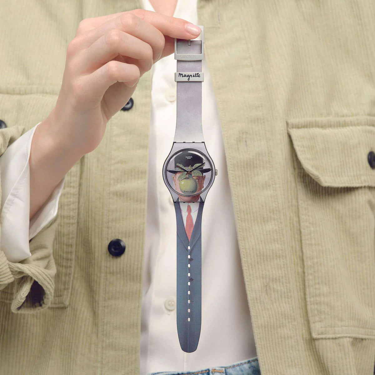 Swatch wristwatch worn on a shirt with art dial, green hands, and light gray strap