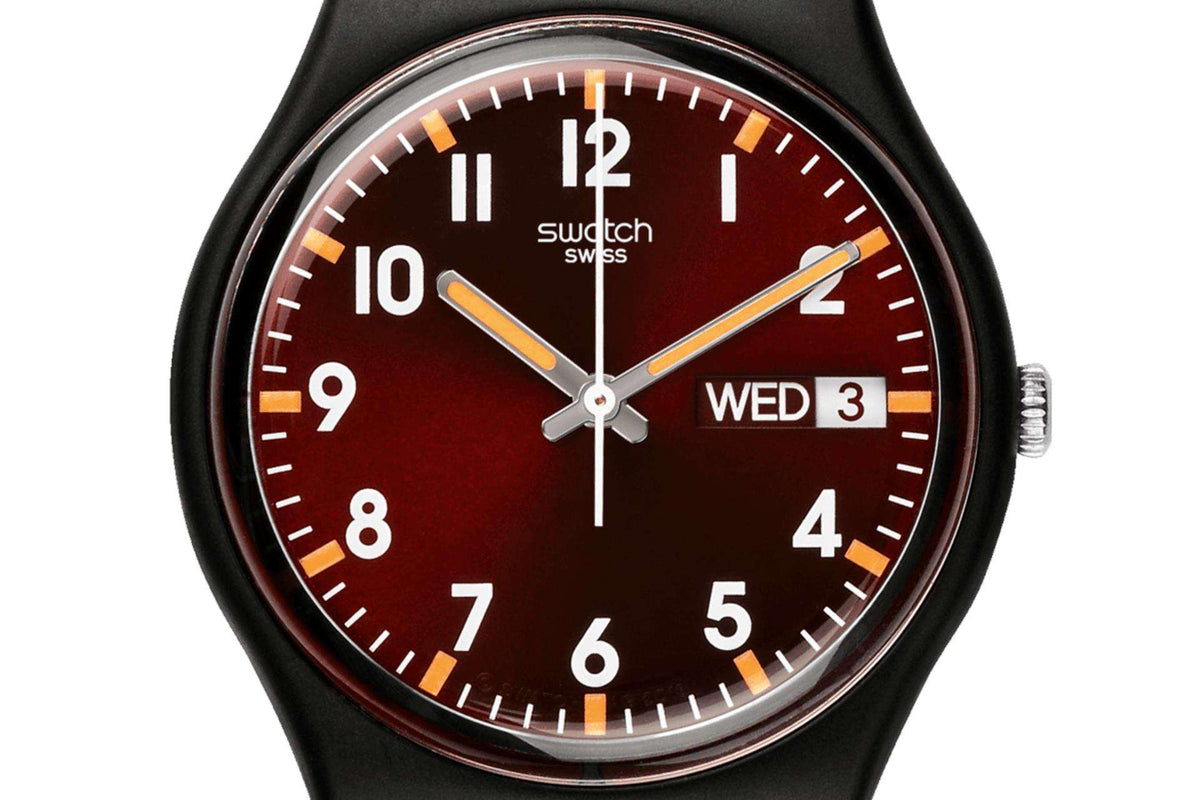Red dial wristwatch close-up with black strap, gold hands, day-date window reading Wed 3