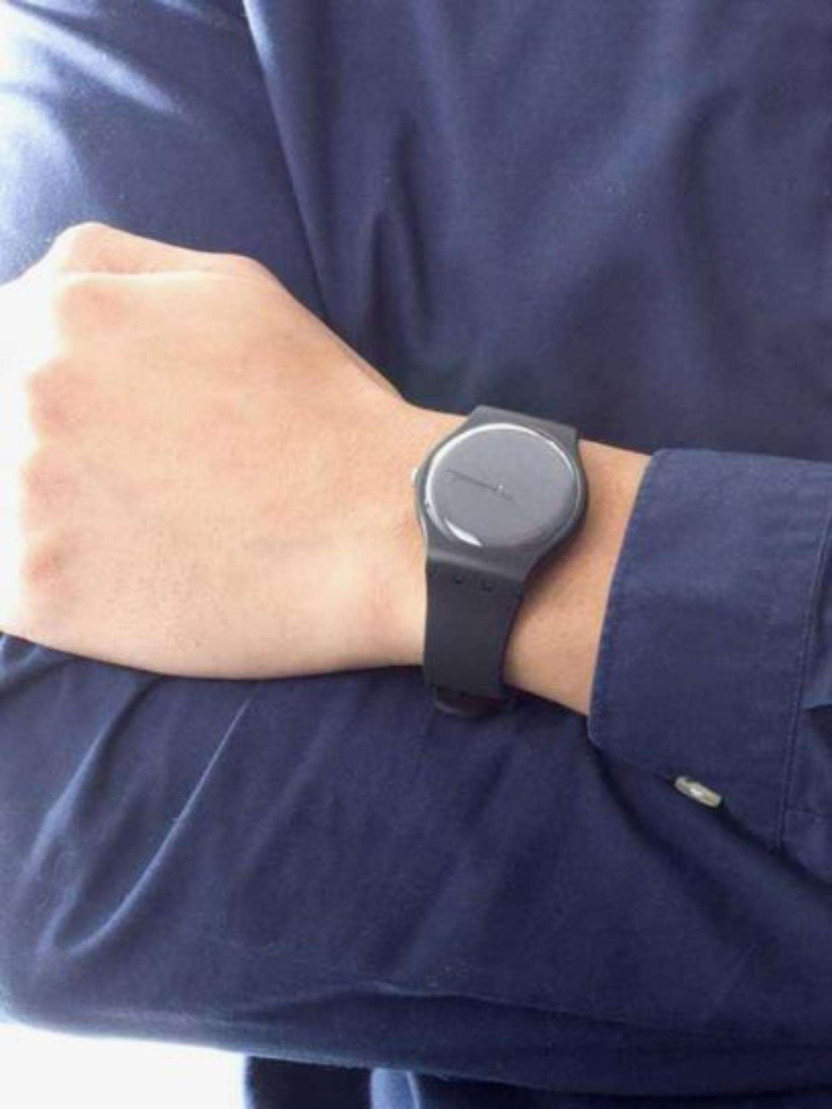 Swatch black silicone strap watch on wrist with dark round face