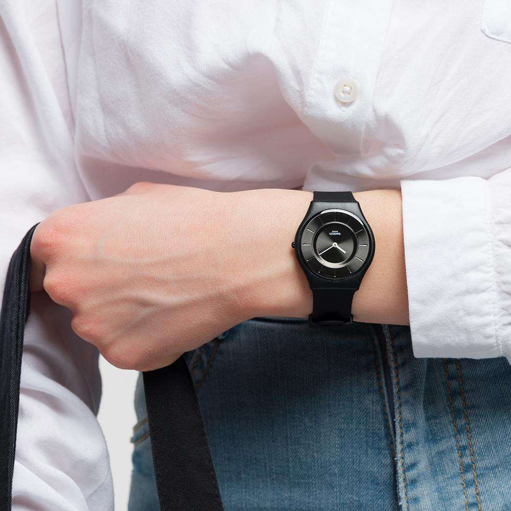 Men's black wristwatch with round dial and light hands, worn with denim