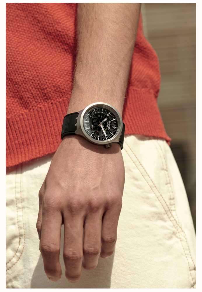 Men's Swatch Swiss watch worn on wrist, black dial with visible gears and black rubber strap