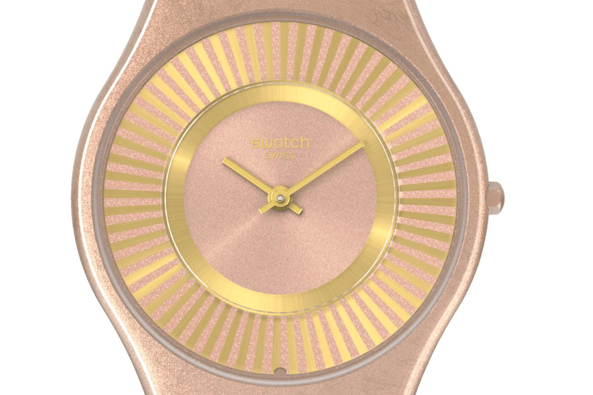 Swatch quartz watch close-up: round tawny dial, gold bezel, sunburst stripe markings
