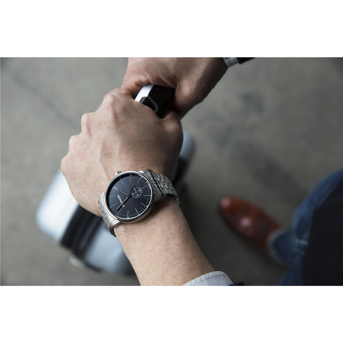 Wristwatch worn on arm: black dial subdials with silver hands and stainless bracelet.