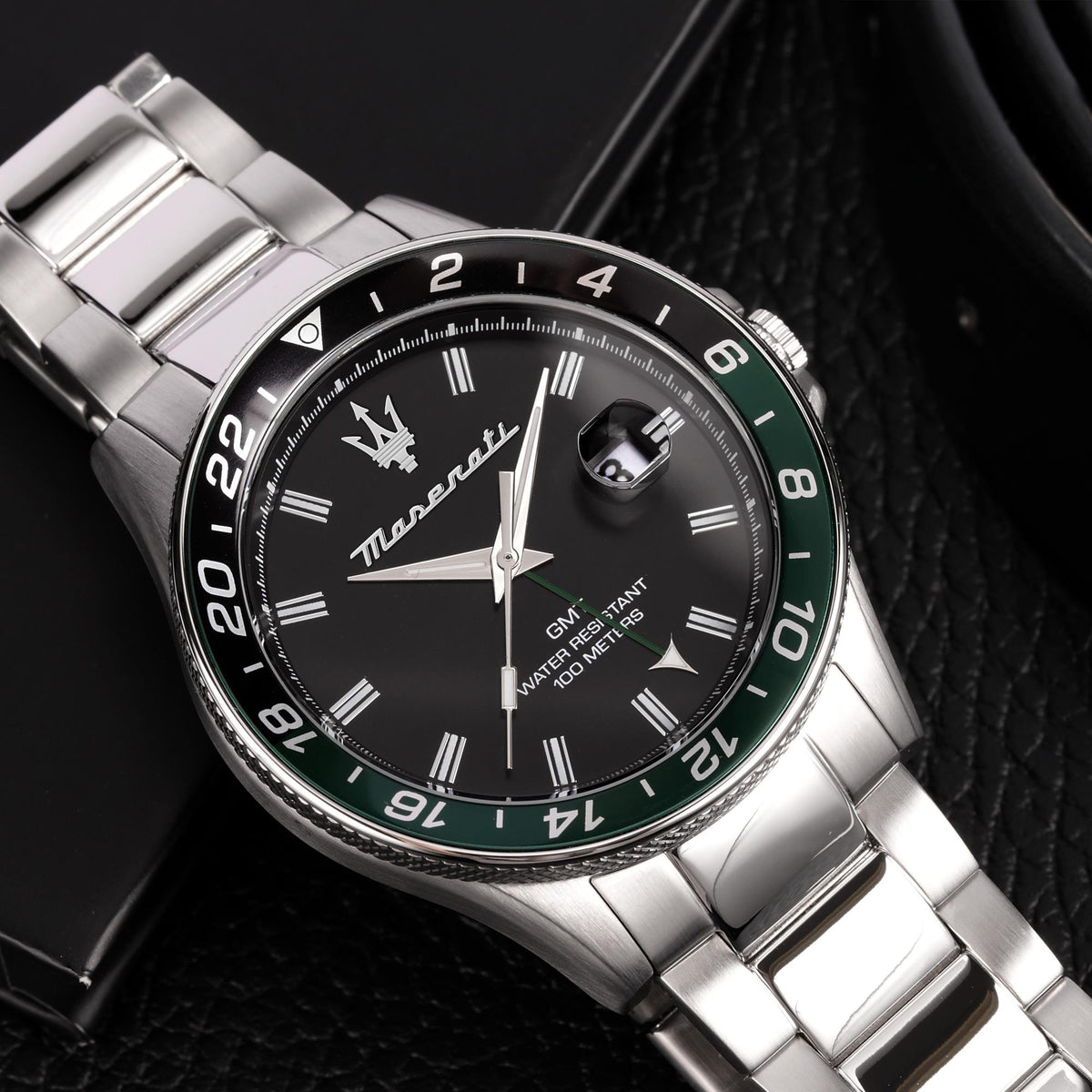 Close-up Maserati GMT quartz watch: black dial, steel case, green bezel accents.