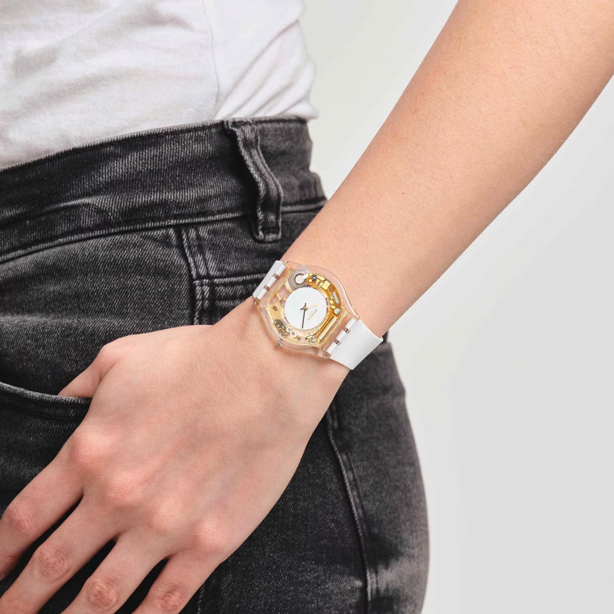 Swatch quartz watch on wrist, white strap and transparent case with gold accents