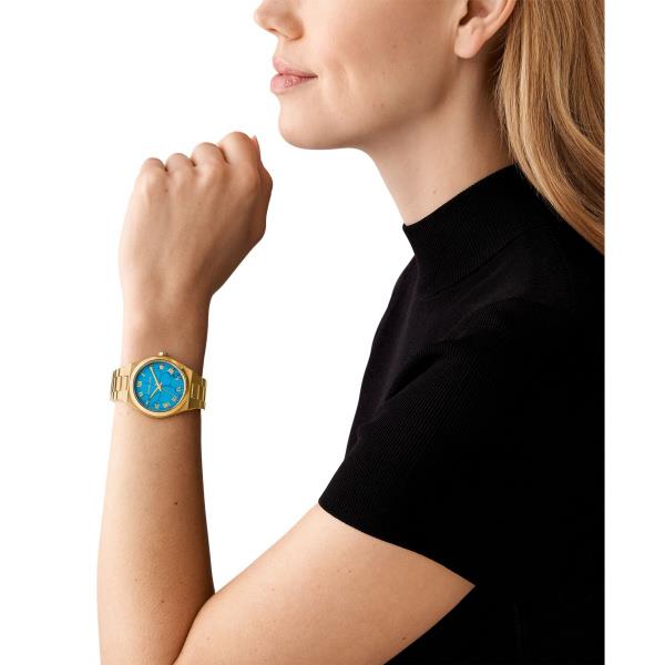 Gold-tone women’s wrist watch with blue dial worn on wrist over a dark shirt.
