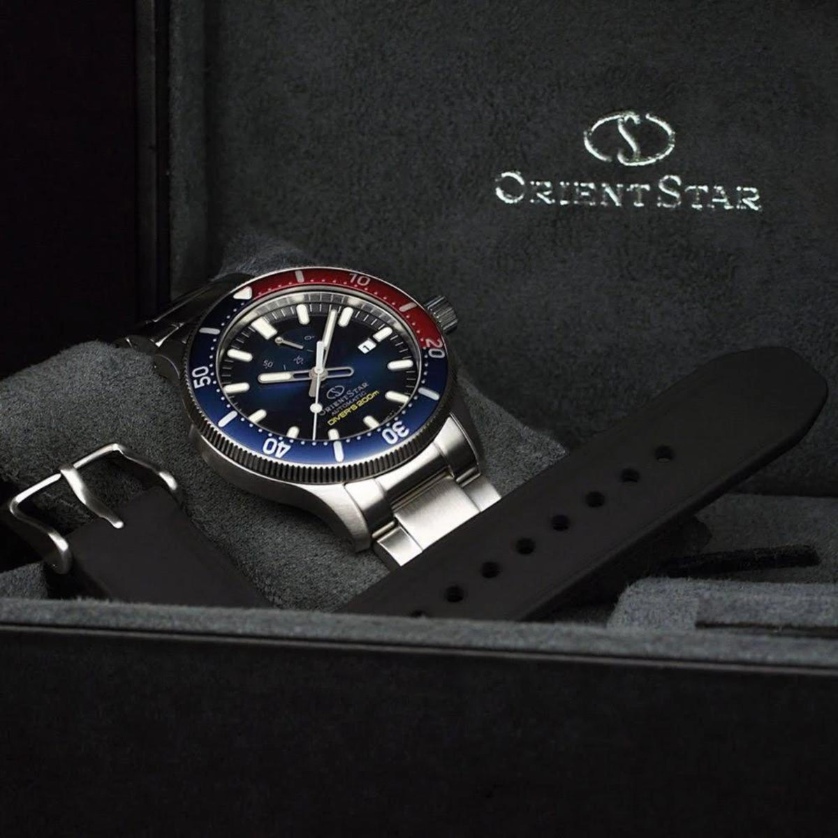 Orient Star diver watch on gray cushion, blue dial, steel case, red/blue rotating bezel
