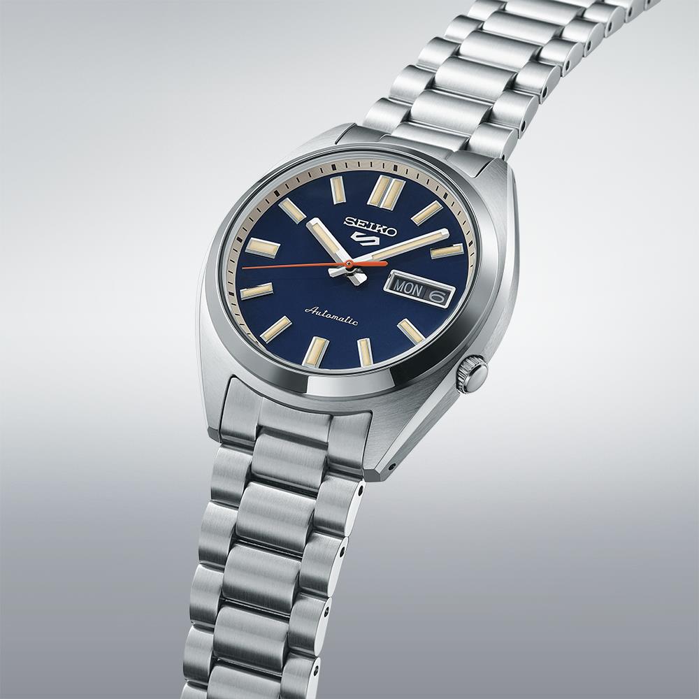 Seiko 5 Sports SRPK87K1 watch against grey background, displaying its case profile and multi-link bracelet.