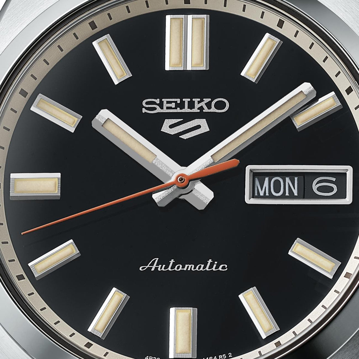 Close-up of Seiko 5 Sports SNXS watch dial, highlighting the Seiko logo, automatic text, textured hands, and day-date window.