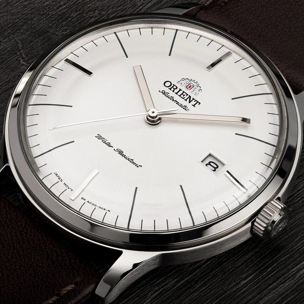 Men's automatic wrist watch close-up: white dial with baton markers, date window at 3