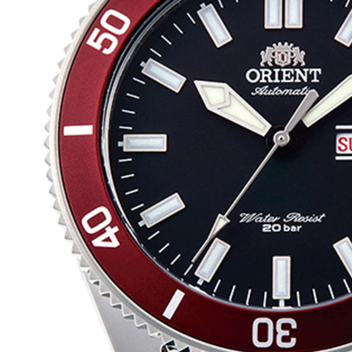Close-up of automatic watch dial with black face, red bezel ring, luminous hour markers.