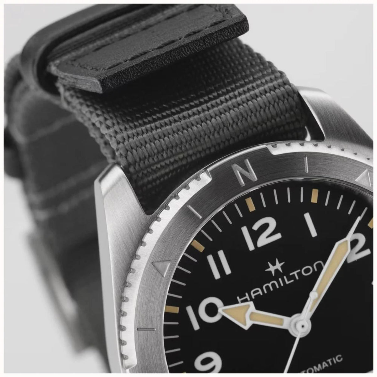 Black dial watch detail with NATO strap, gold markers, and silvertone bezel