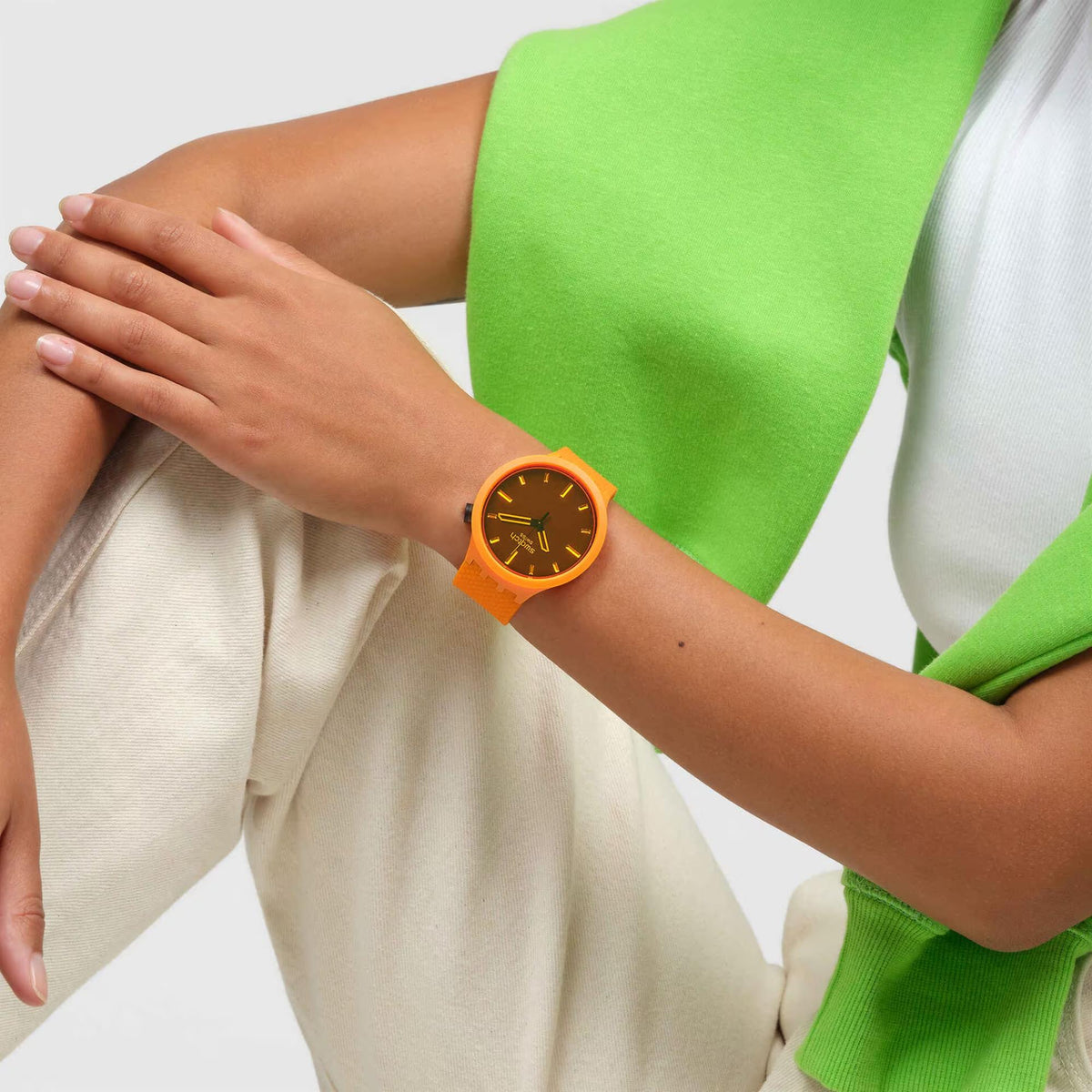 Orange Swatch watch on wrist with dark dial and gold hands; orange silicone strap