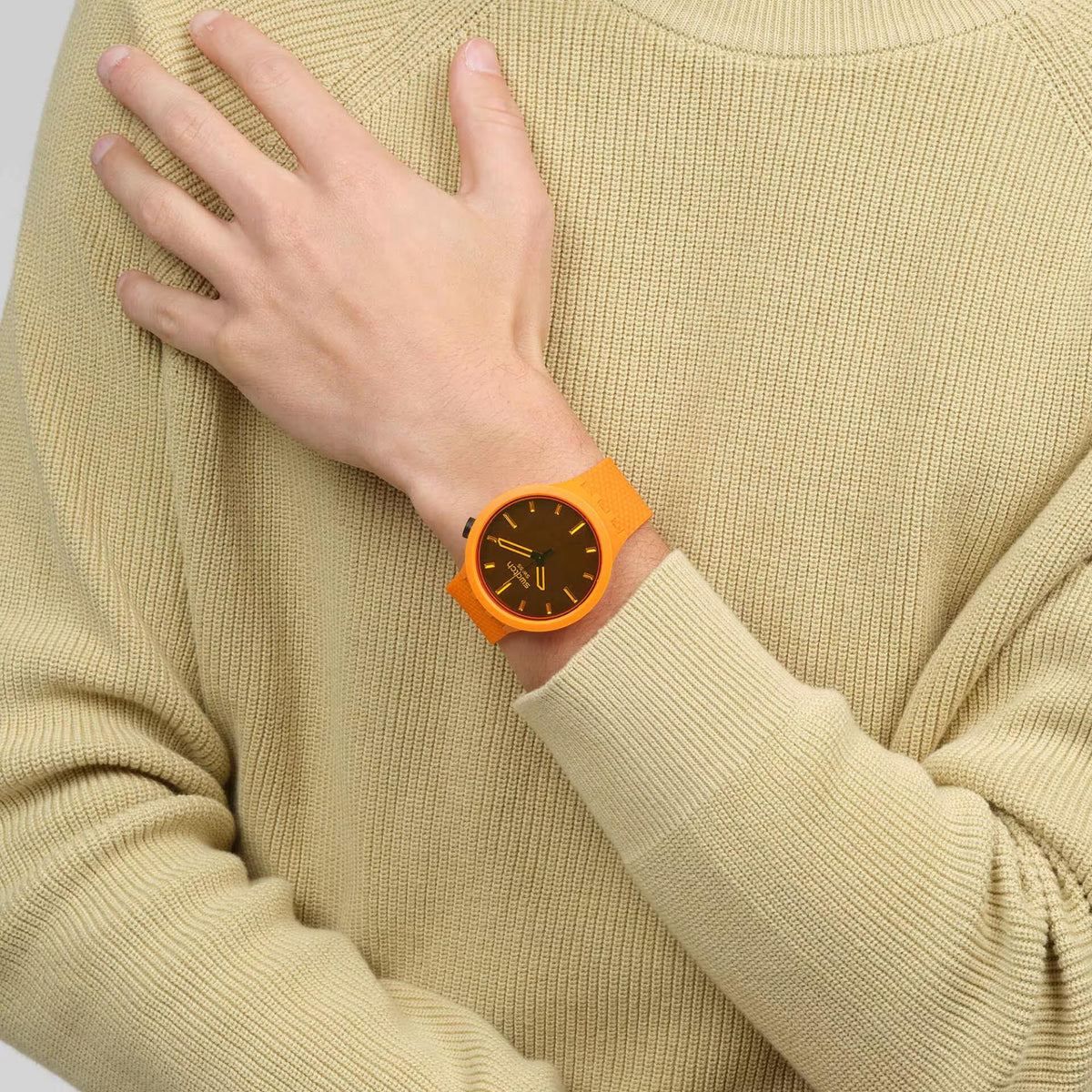 Orange Swatch watch on sweater cuff with dark dial, gold hands, and orange silicone strap
