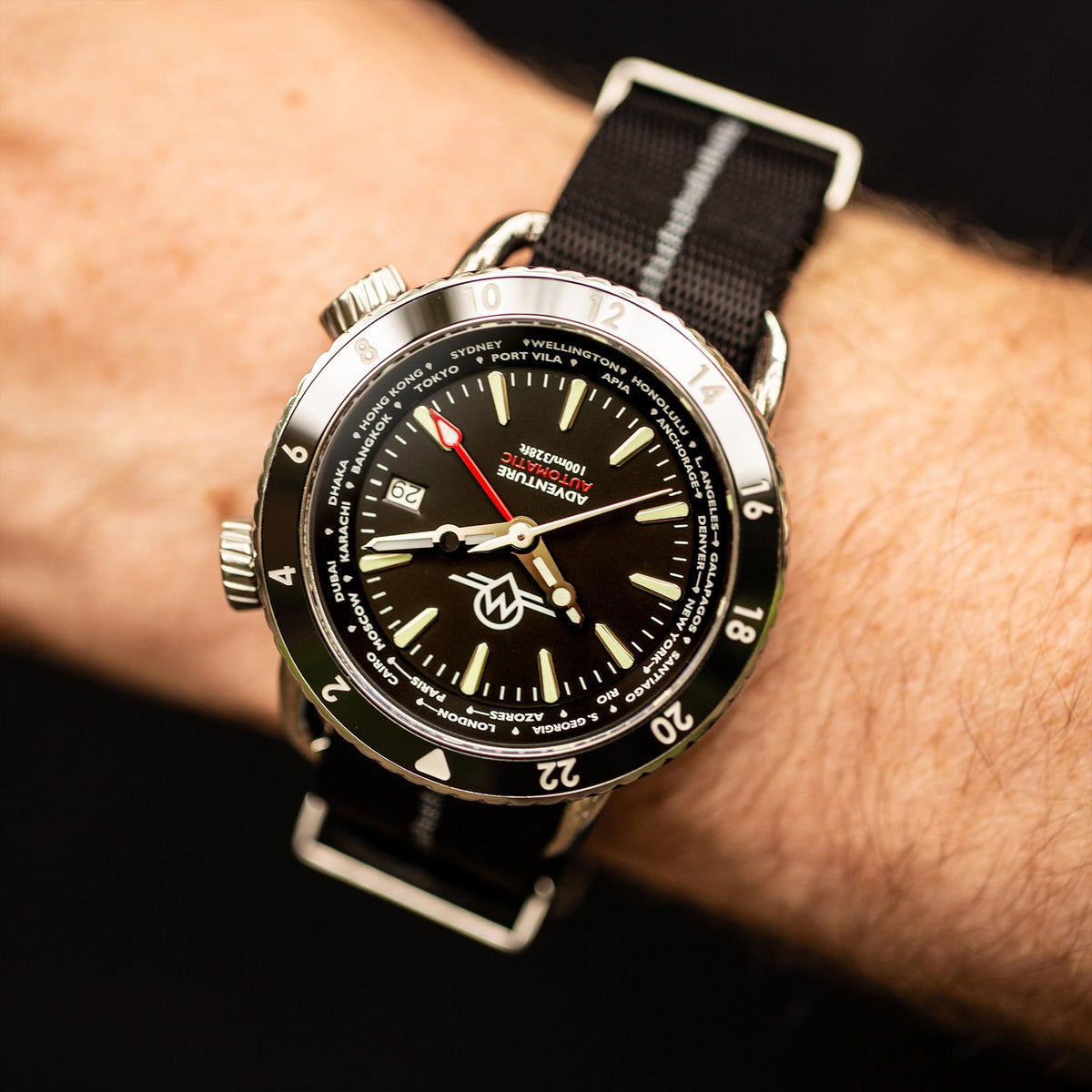 Men's automatic watch on wrist with black dial, red seconds hand, green luminous markers
