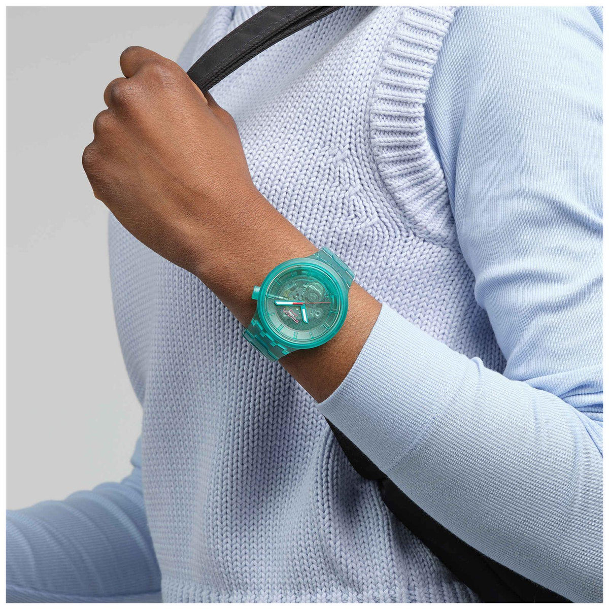 Turquoise clear-case wristwatch on sleeve, round dial with three hands