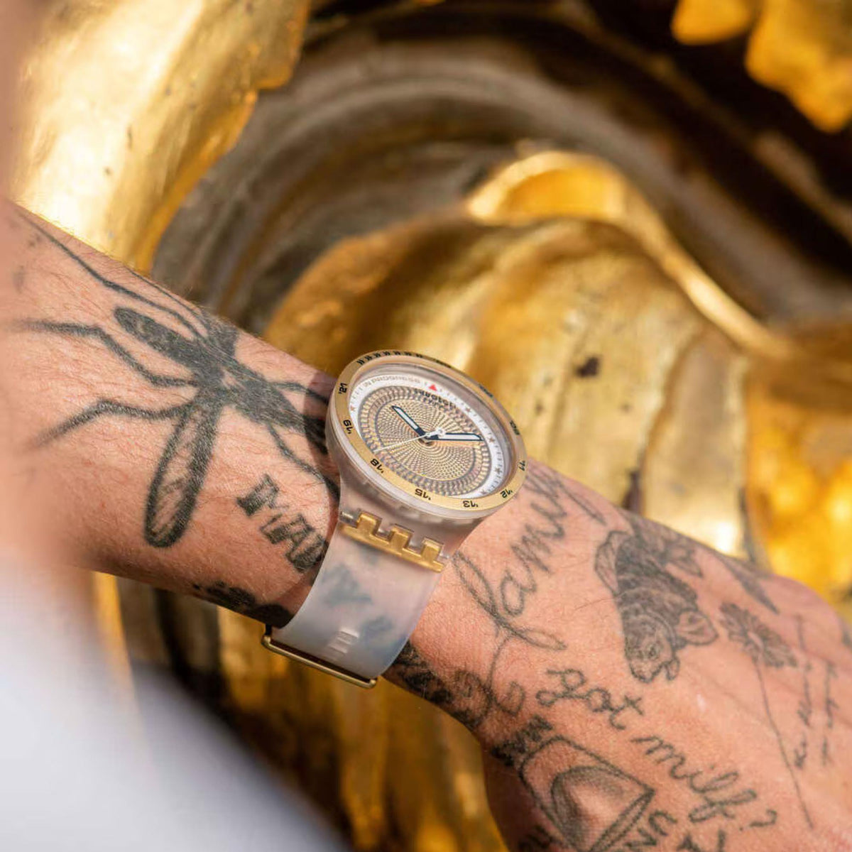 Gold-tone mens watch with textured gold dial and white silicone strap on wrist